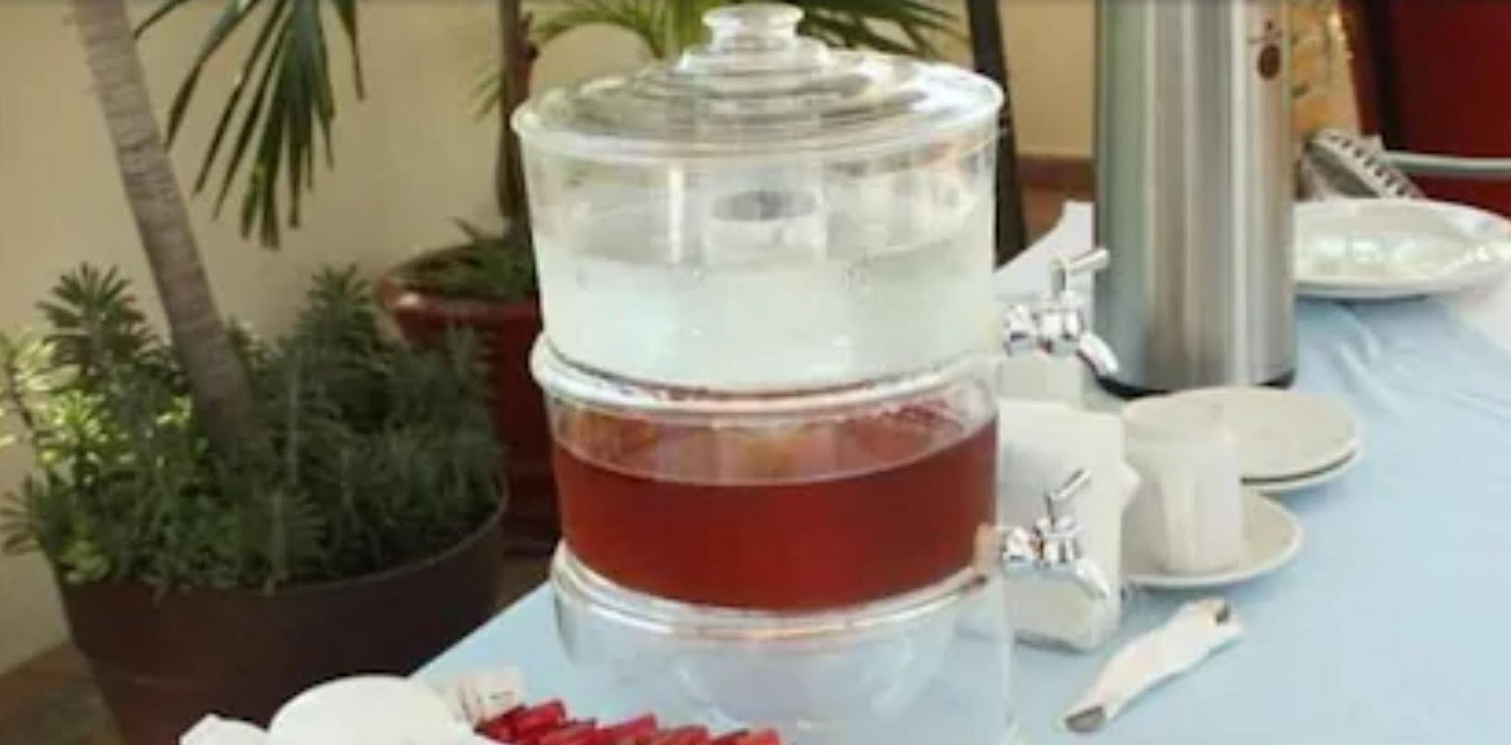 A water dispenser with a clear container, a white cup, and a plate with food items on a table.
