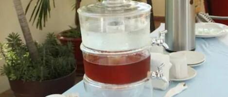 Een waterdispenser met een transparante container, een witte beker en een bord met etenswaren op een tafel.