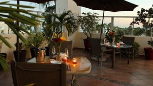 An outdoor dining area with tables, chairs, potted plants, and a view of the cityscape.