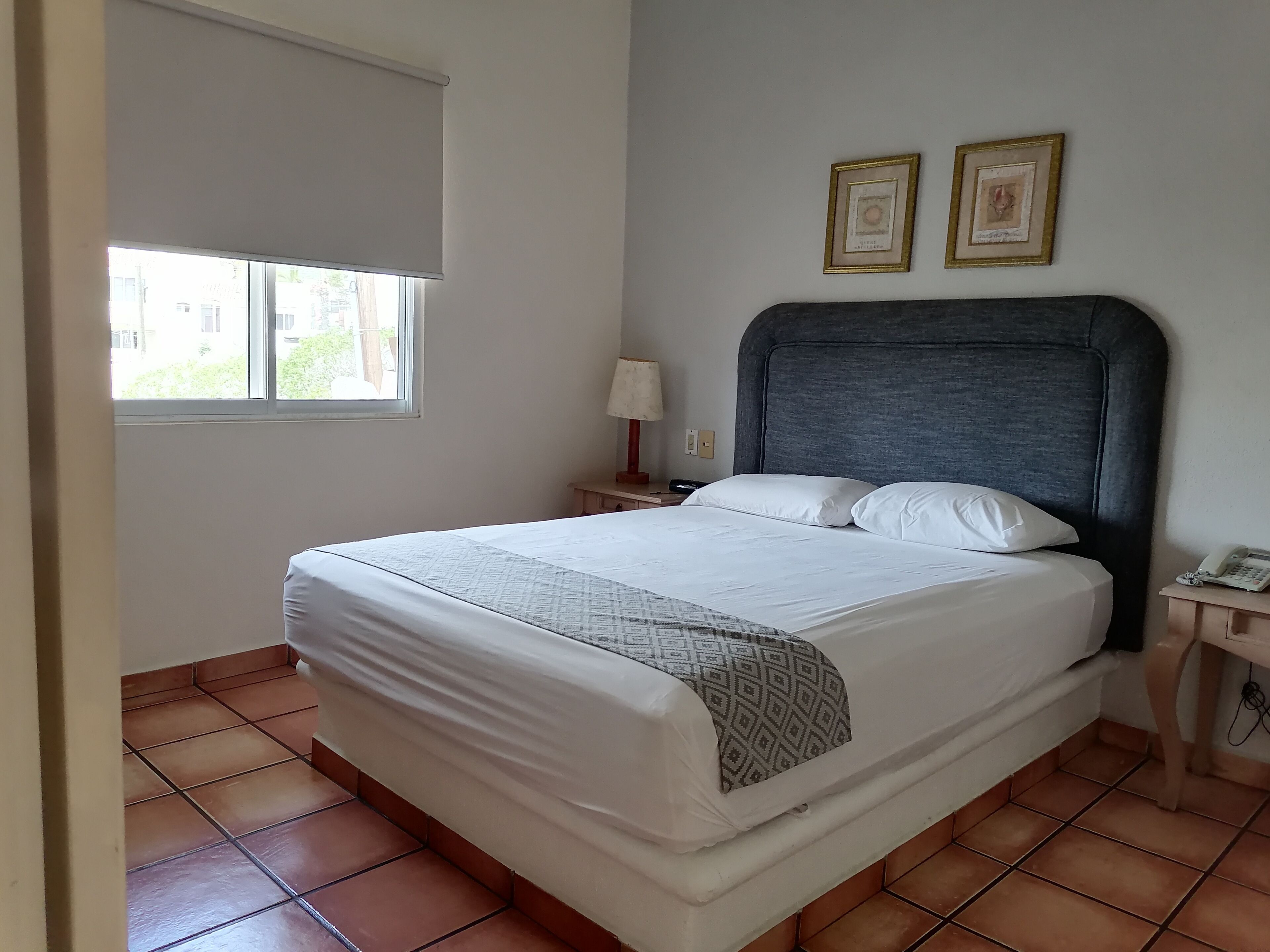 A hotel room with a bed, a nightstand, a lamp, and two framed pictures on the wall.