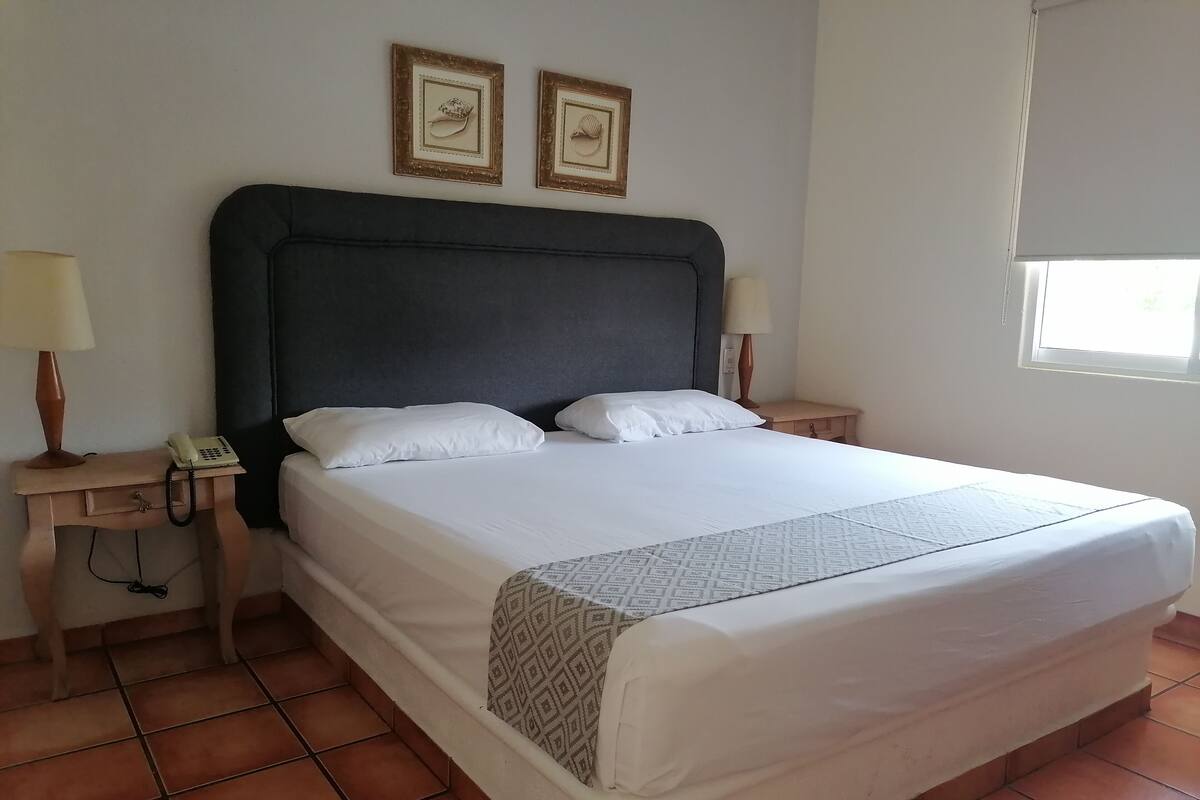 Una cama bien hecha con sábanas blancas, un cabecero oscuro y dos cuadros en la pared.