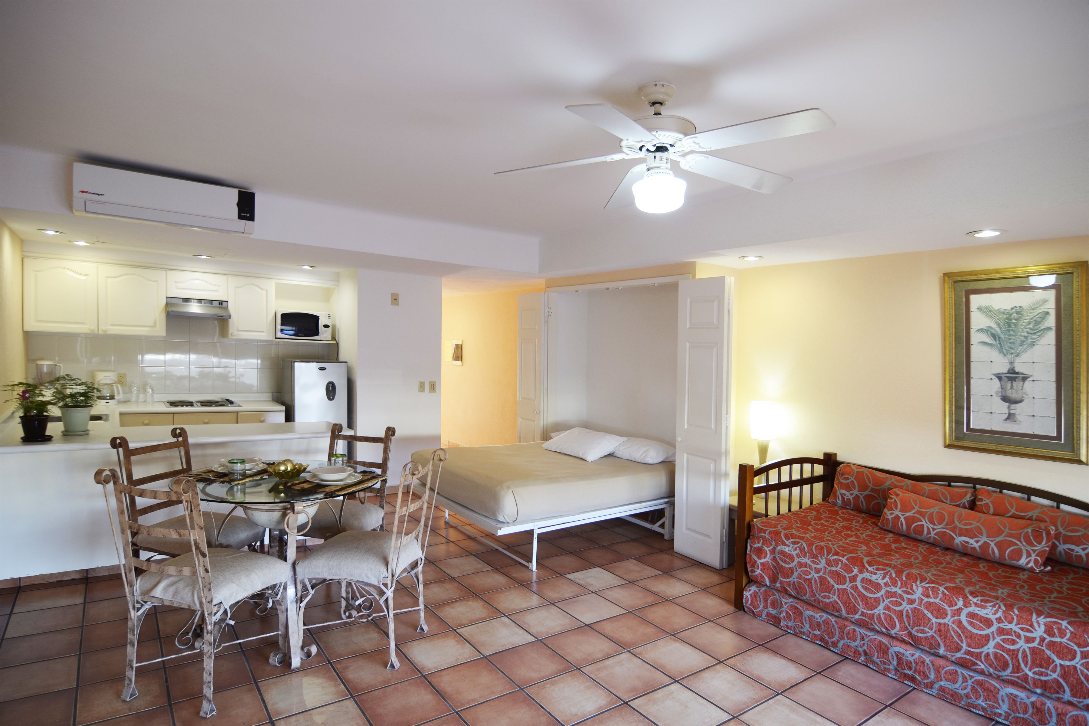 A compact living space with a kitchenette, a dining table with chairs, a bed, and a sofa.