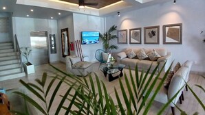 A modern living room with a sofa, armchairs, a coffee table, and a TV. There is a staircase leading to another level.