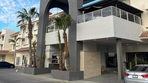 A hotel entrance with a prominent archway, a covered balcony, and palm trees.
