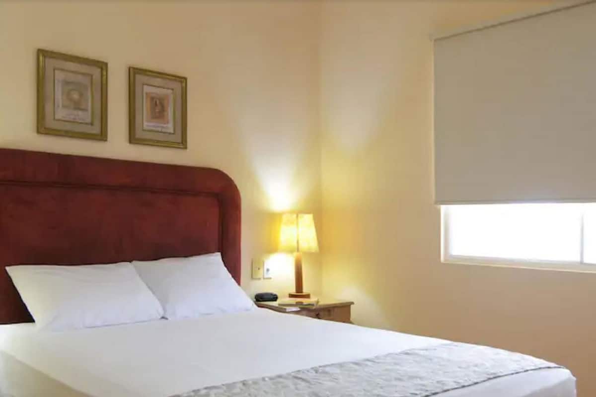Una habitación de hotel con una cama, una mesita de noche, una lámpara y dos cuadros en la pared.