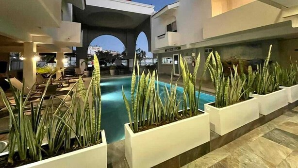 An indoor pool area with lounge chairs and planters, a red dome structure in the background, and a clear view of the sky.