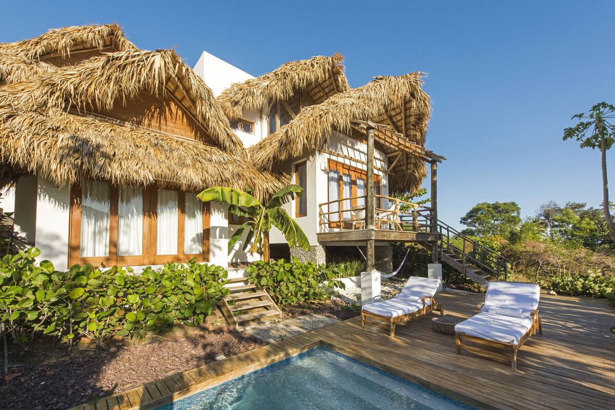 Un resort con piscina, sillas de descanso y un edificio con techo de paja.