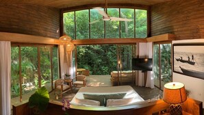 Una habitación amplia con una cama grande, un televisor y vistas al bosque a través de ventanales.
