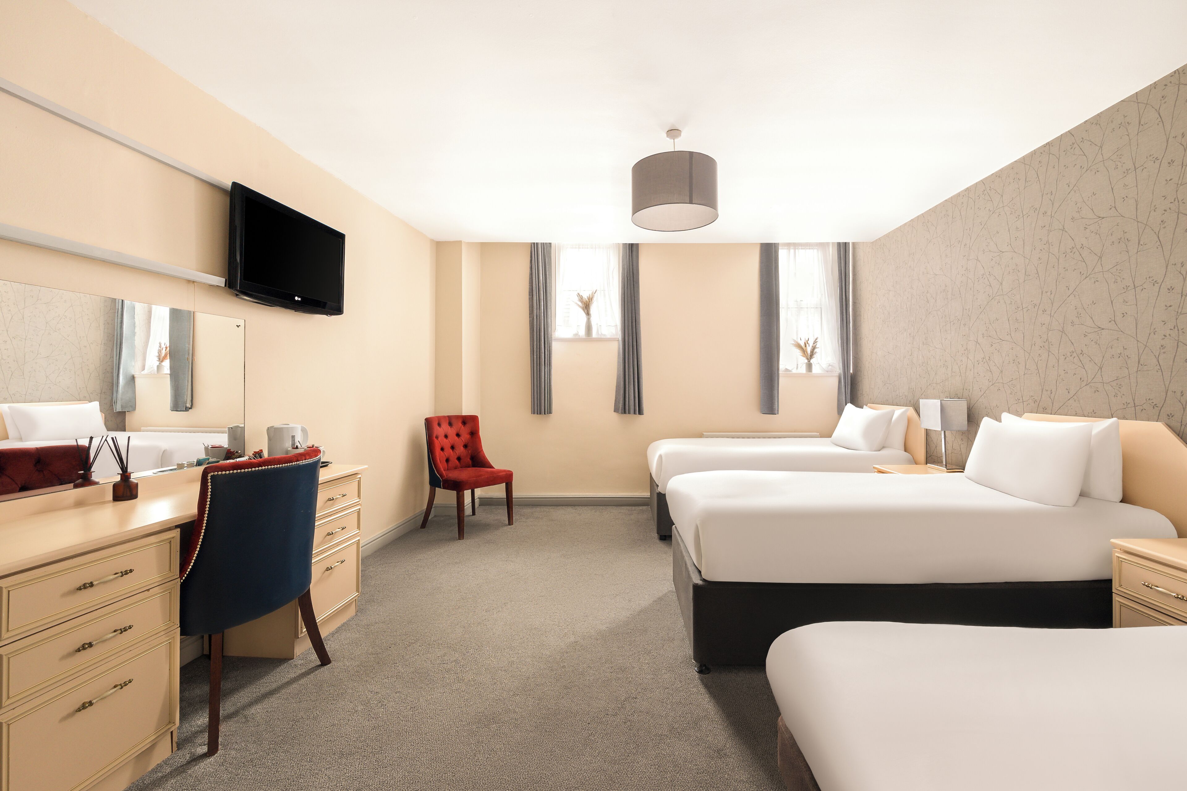 Een hotelkamer met twee bedden, een bureau met stoel, een aan de muur bevestigde televisie en een groot raam met gordijnen.