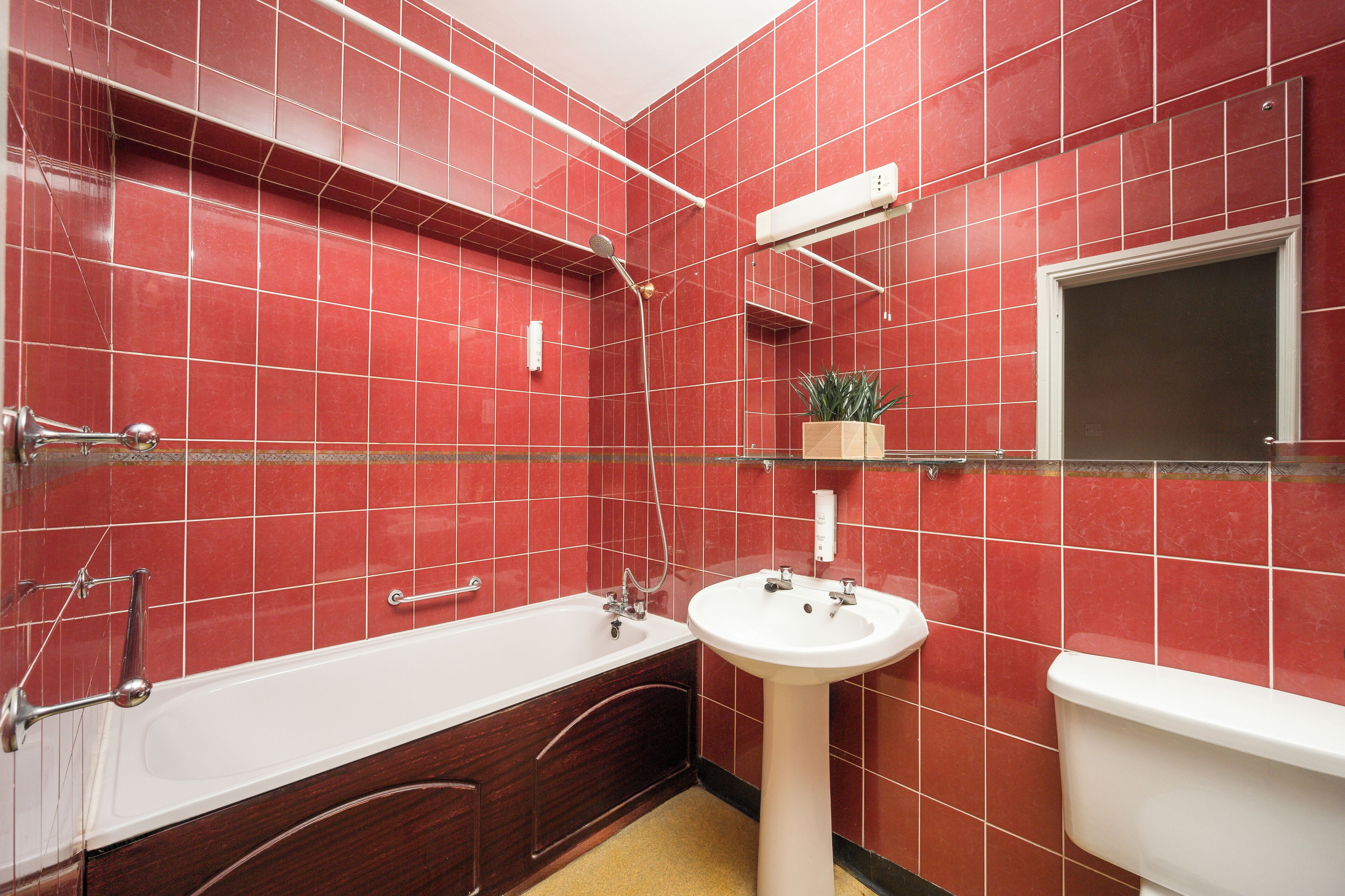 A bathroom with red tiled walls, a white bathtub, a white sink, and a toilet.