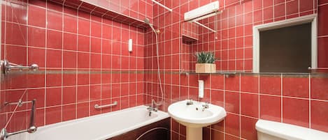 A bathroom with red tiled walls, a white bathtub, a white sink, and a toilet.