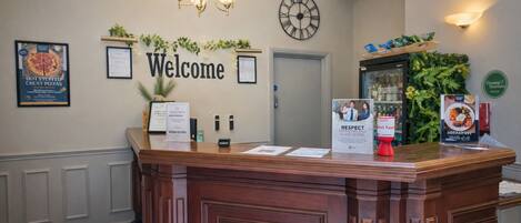 Un mostrador de recepción con un cartel de 'Welcome', certificados enmarcados, un reloj y un cartel que dice 'RESPECT'.