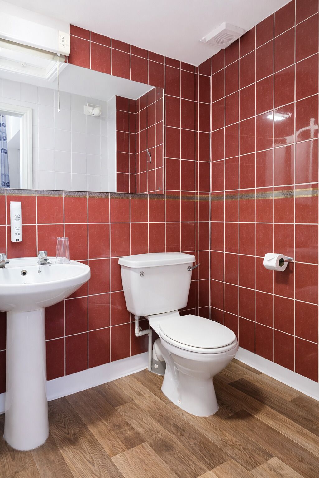 Un baño con paredes de azulejos rojos, un lavamanos blanco y un inodoro.