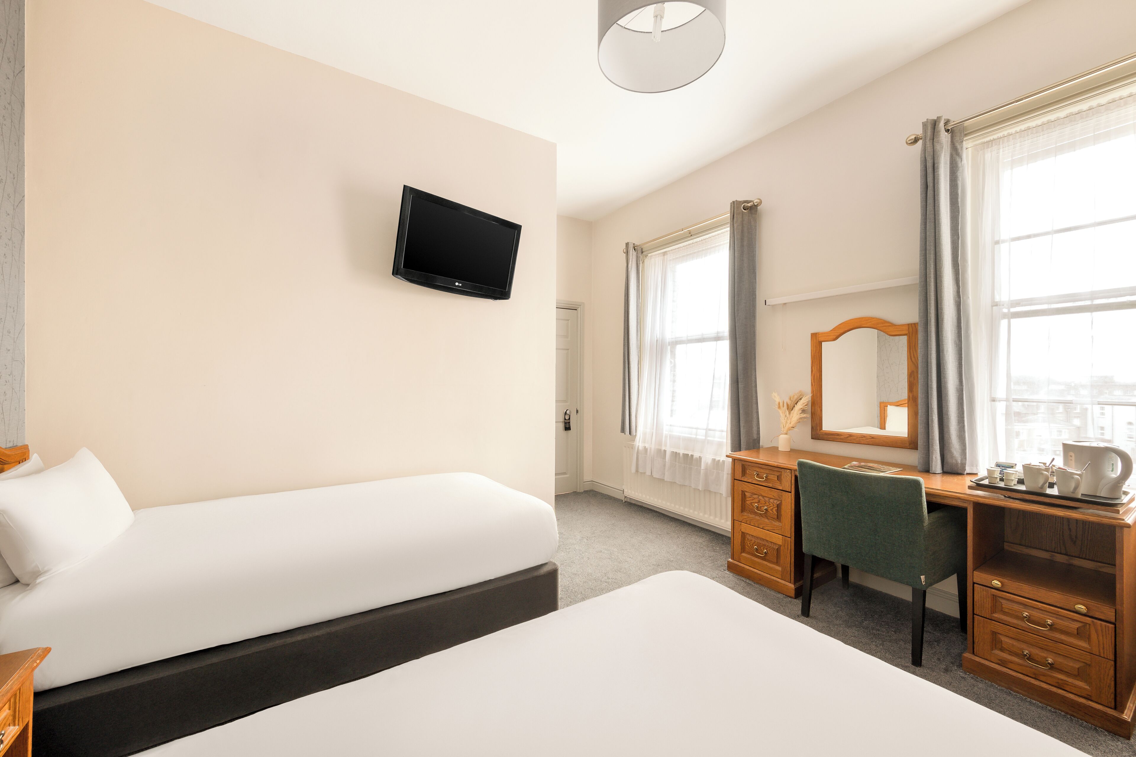 Une chambre d’hôtel comprenant un lit, un bureau avec une chaise, une télévision, une fenêtre avec des rideaux et un miroir.