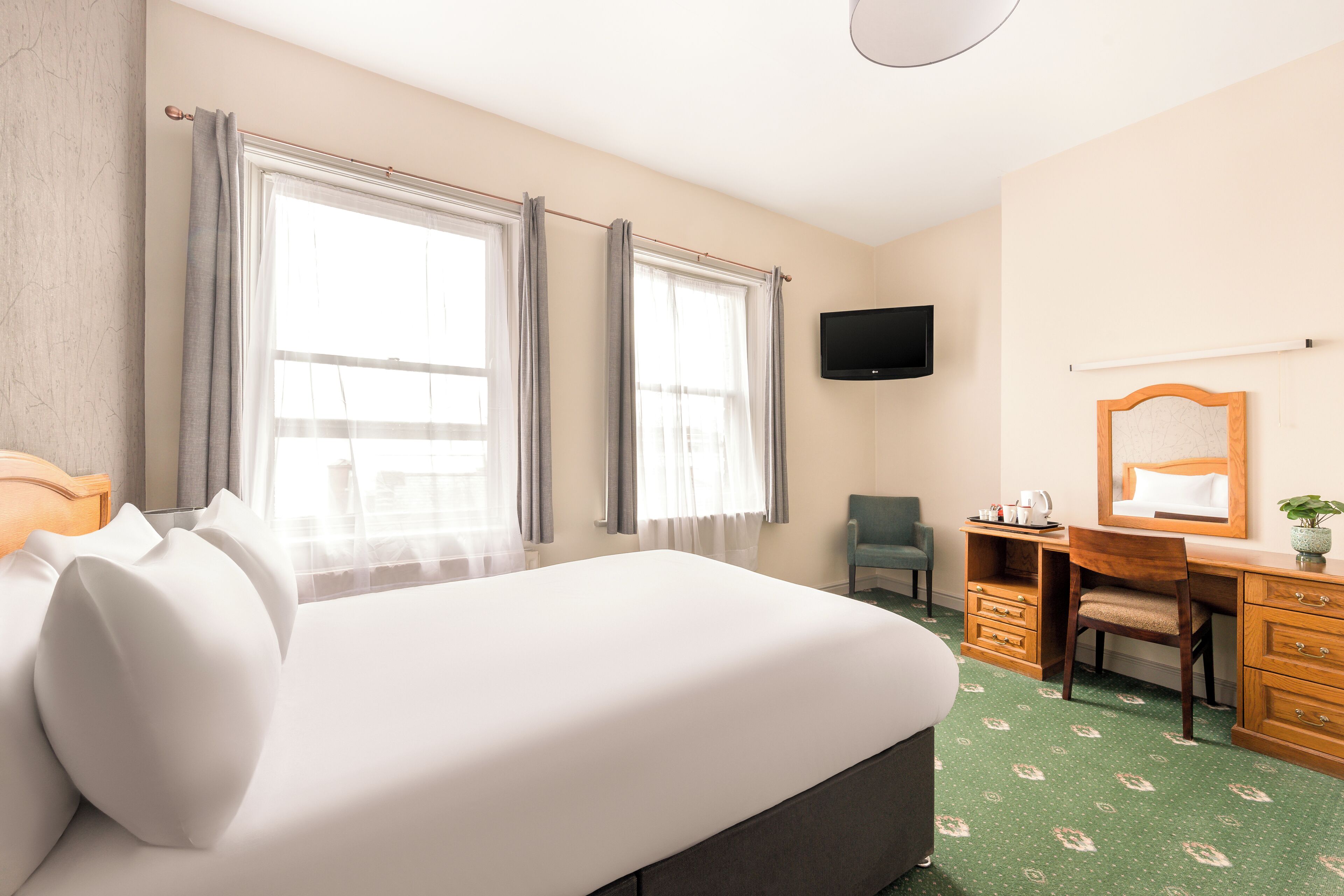 Une chambre d’hôtel avec un grand lit, un bureau, une chaise, une télévision et une fenêtre avec des rideaux.