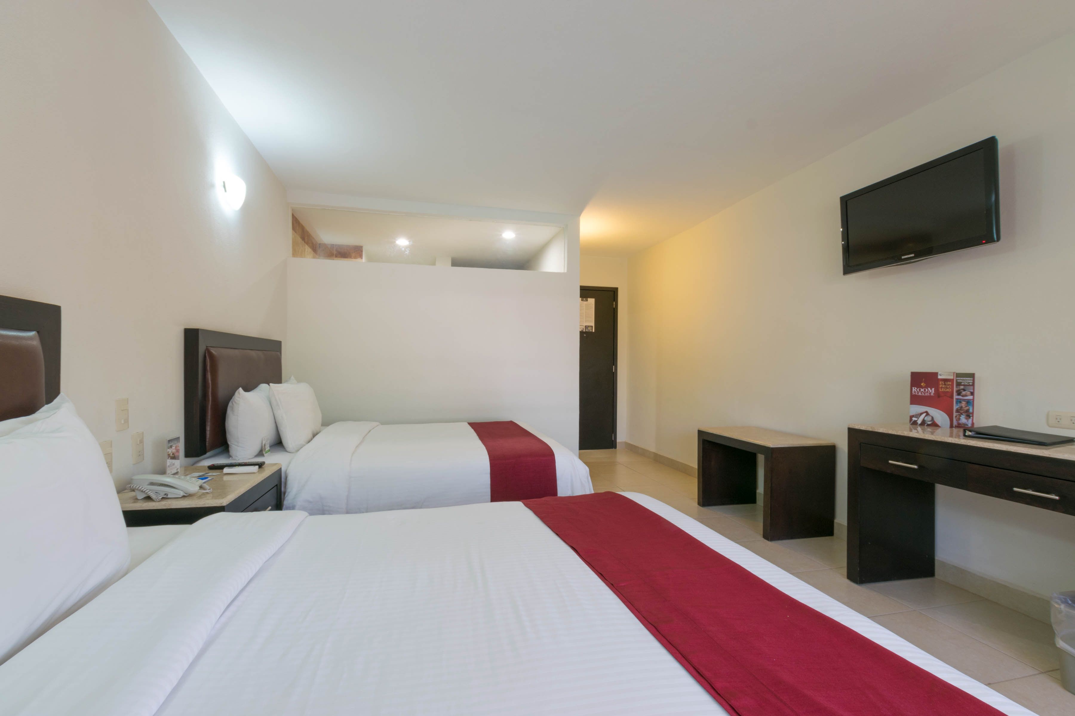 Habitación de hotel con dos camas, un escritorio, una silla, un televisor montado en la pared y una ventana pequeña.