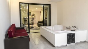 A modern bathroom with a large bathtub, a red sofa, and a glass door leading to a living area.