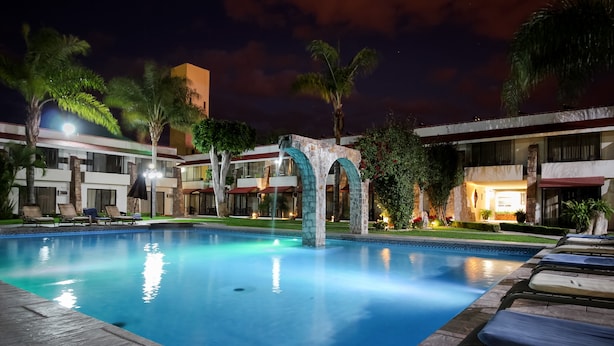 A swimming pool with lounge chairs, palm trees, and a building with stone arches.