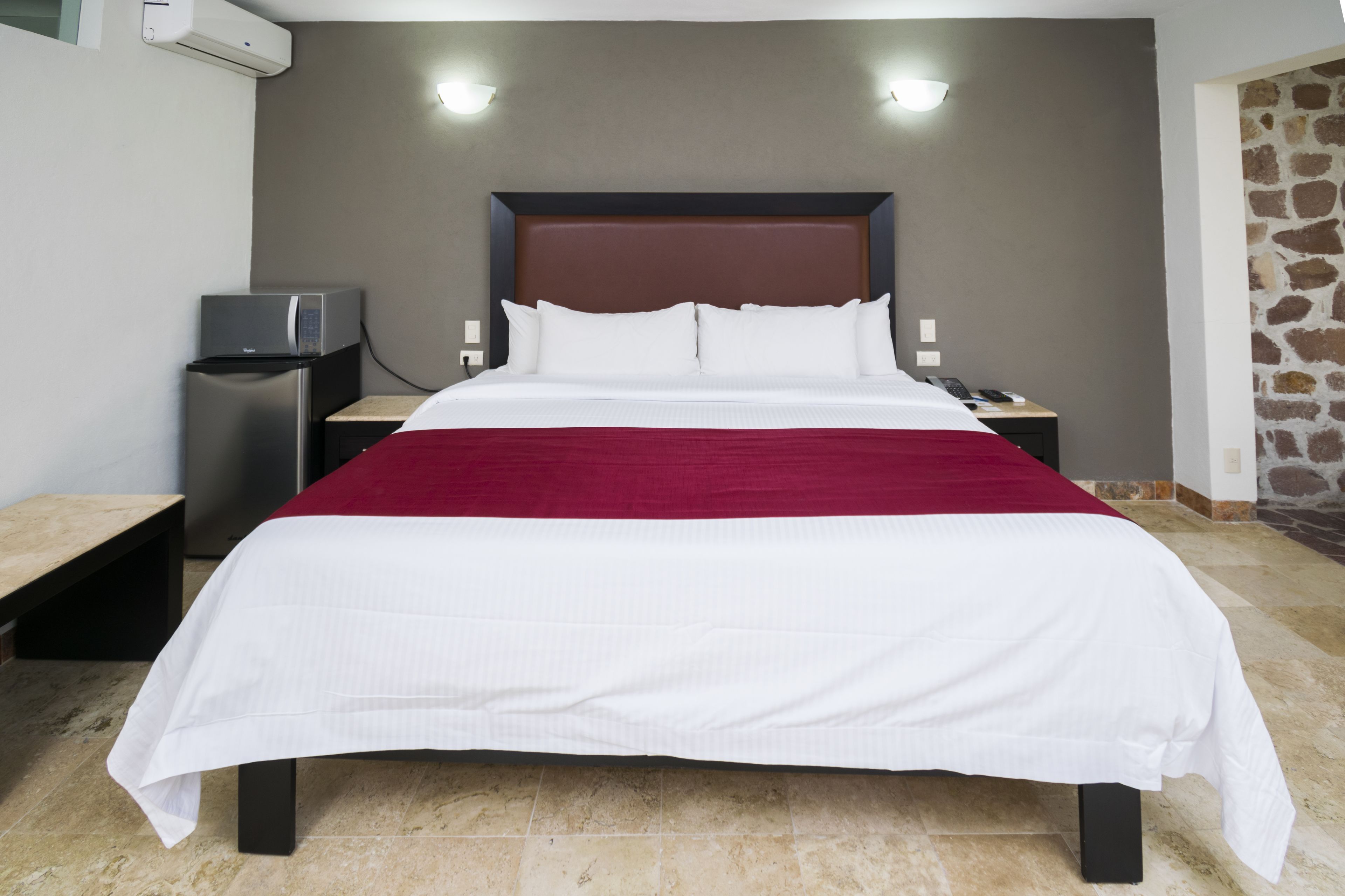 Habitación de hotel con una cama grande, un escritorio pequeño con una computadora y una pared de piedra.