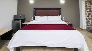 A hotel room with a large bed, a small desk with a computer, and a stone wall.