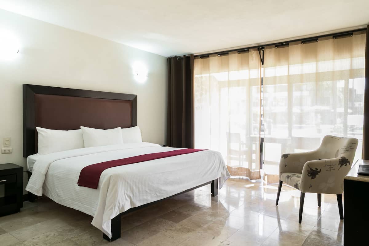 A hotel room with a large bed, a chair, a desk, and a window with curtains.