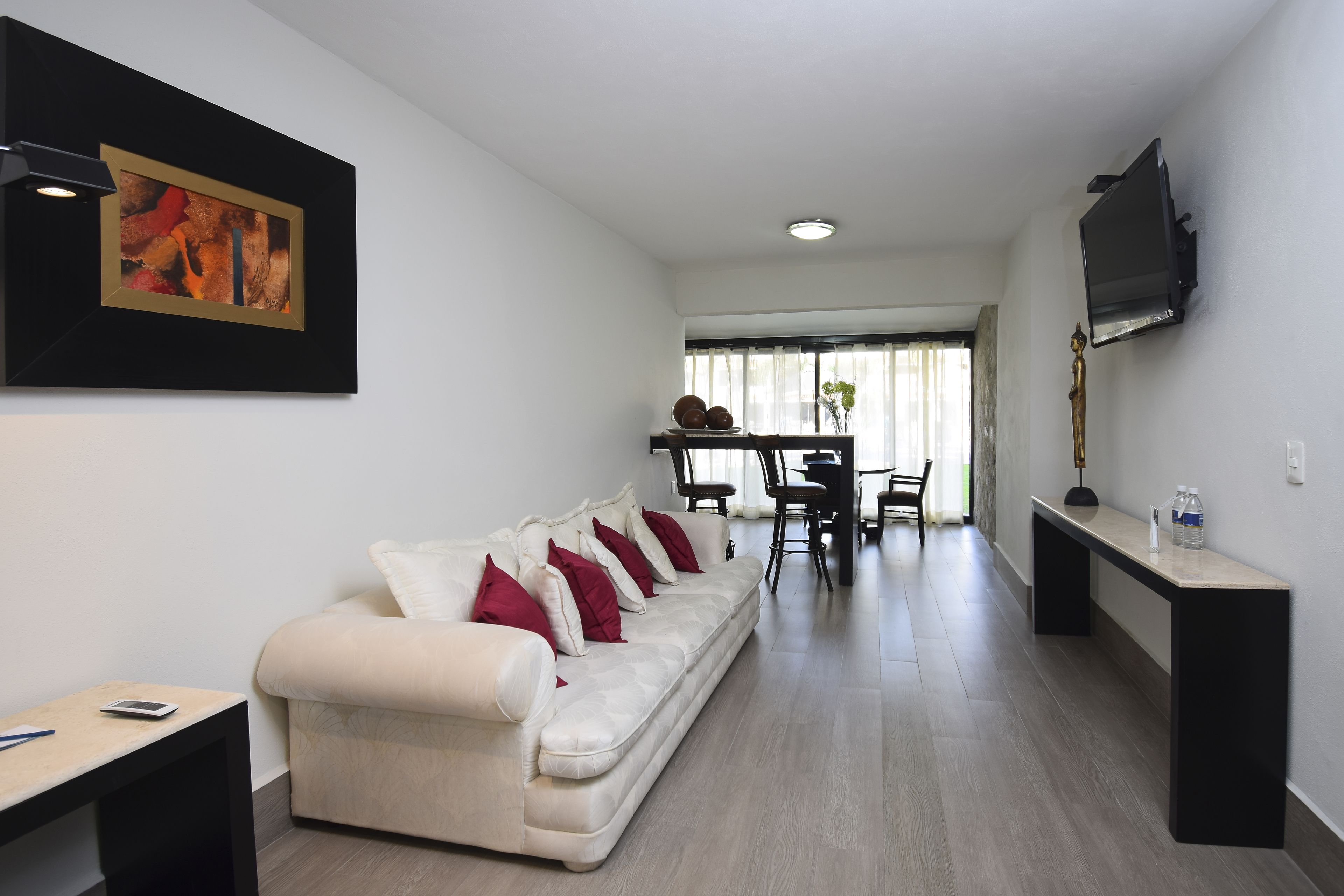 A modern living room with a white sofa, a dining area, and a TV mounted on the wall.