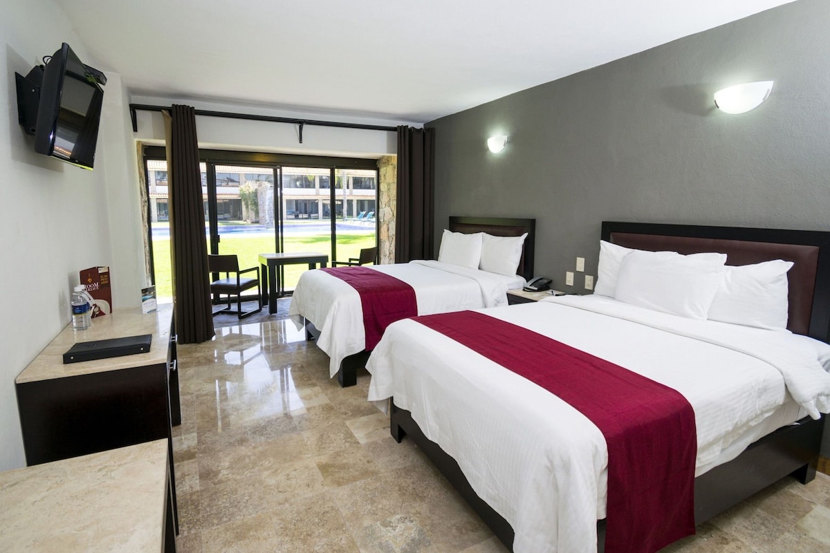A hotel room with two beds, a desk, a chair, and a television.