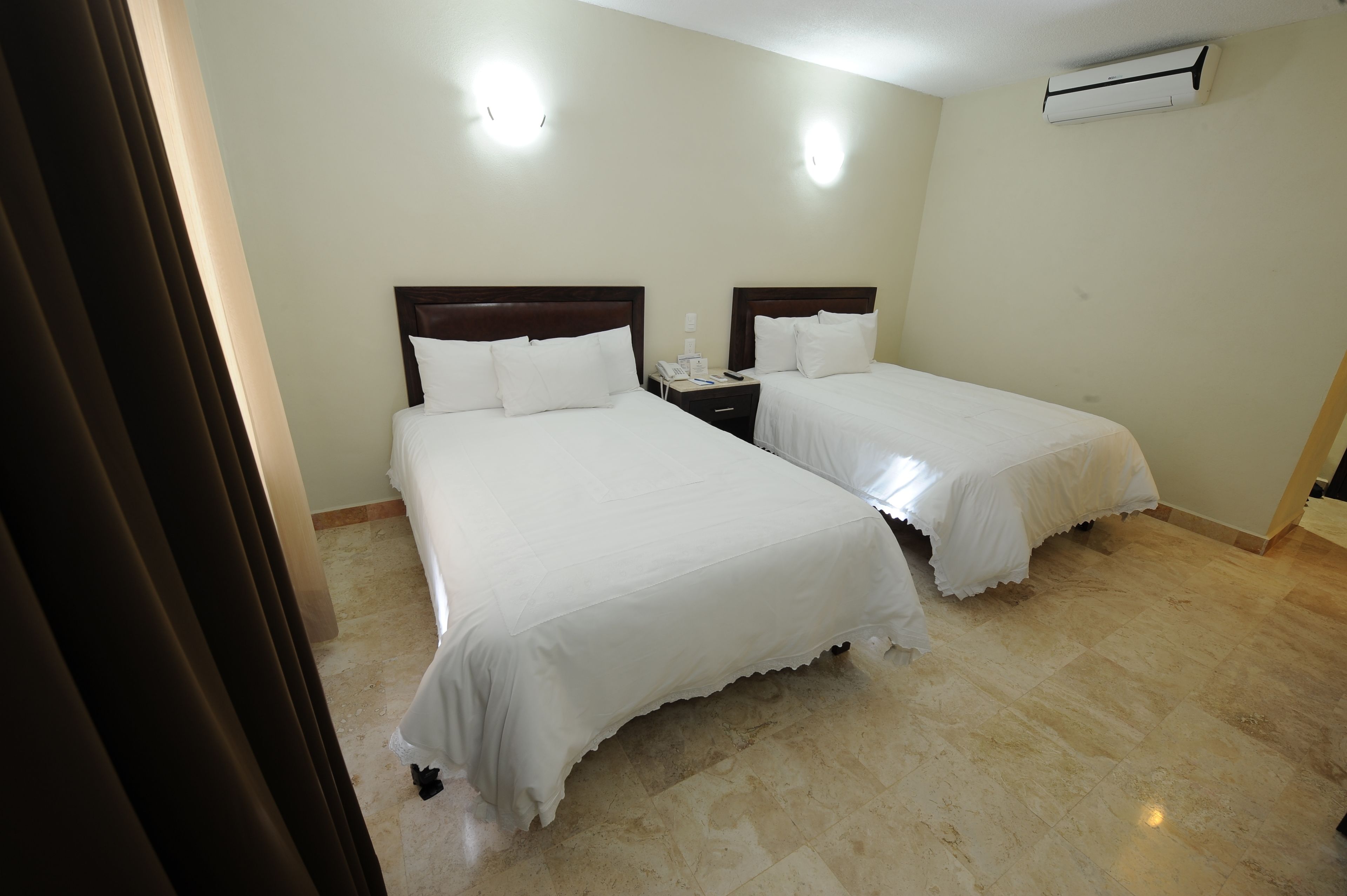 A hotel room with two beds, a nightstand, and a wall-mounted air conditioner.