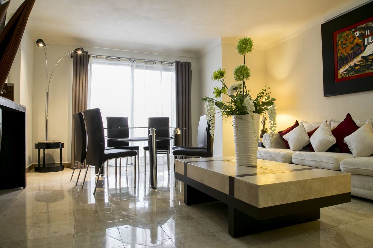 A modern living room with a sofa, a coffee table, and a dining area with chairs and a table.