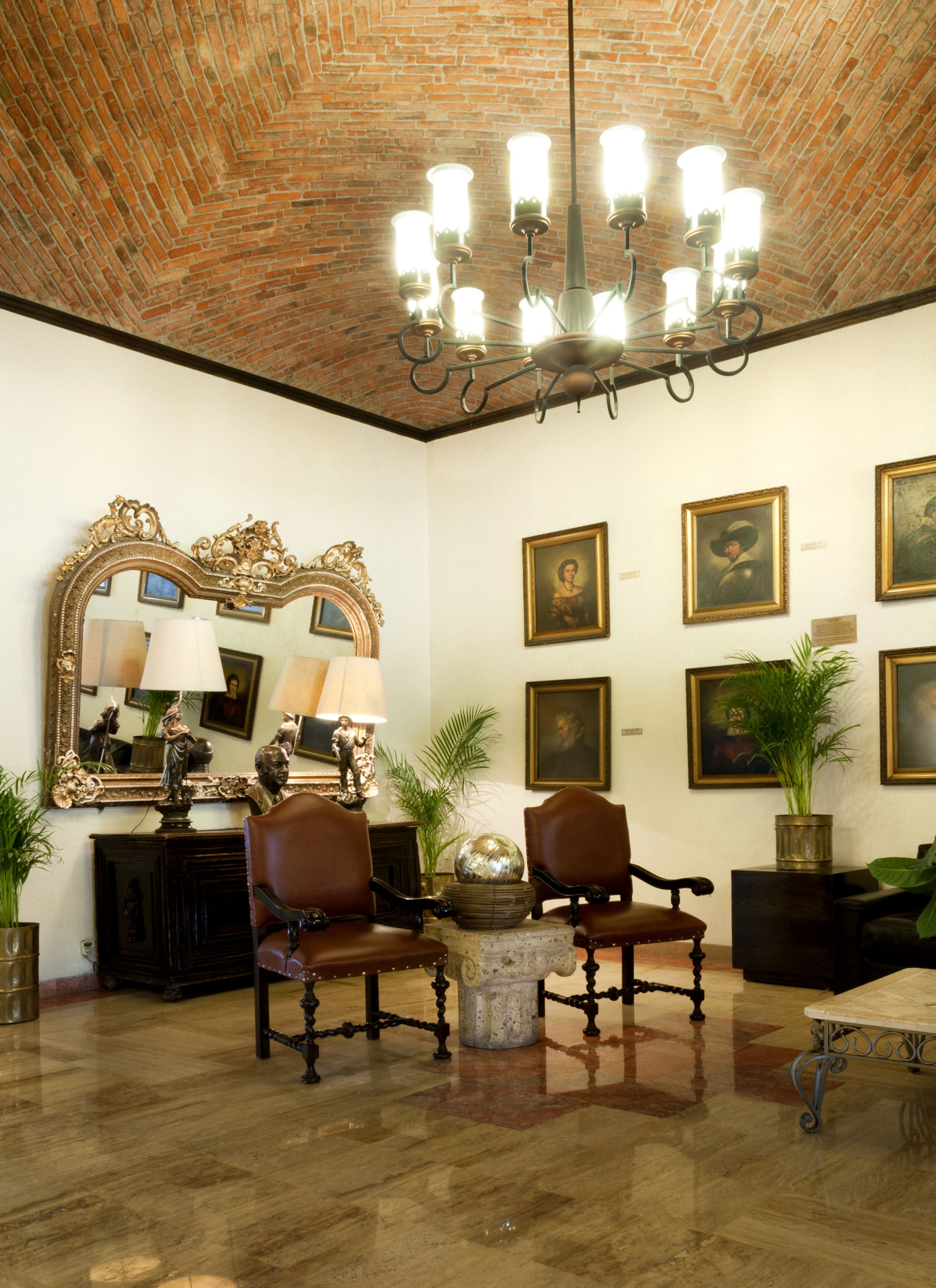 A room with a brick ceiling, a chandelier, a large mirror, and several framed portraits on the wall.