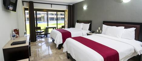 A hotel room with two beds, a desk, a TV, and a view of the outside.