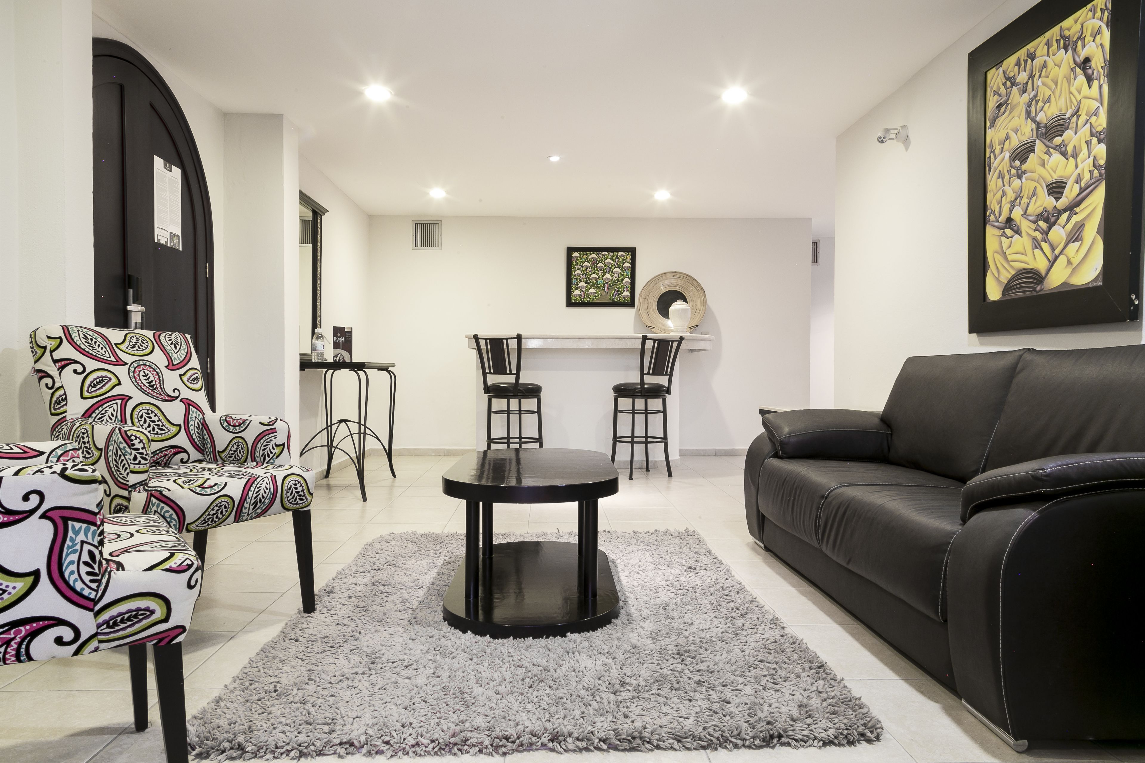 A living room with a black leather sofa, patterned armchairs, a round coffee table, and a gray rug.