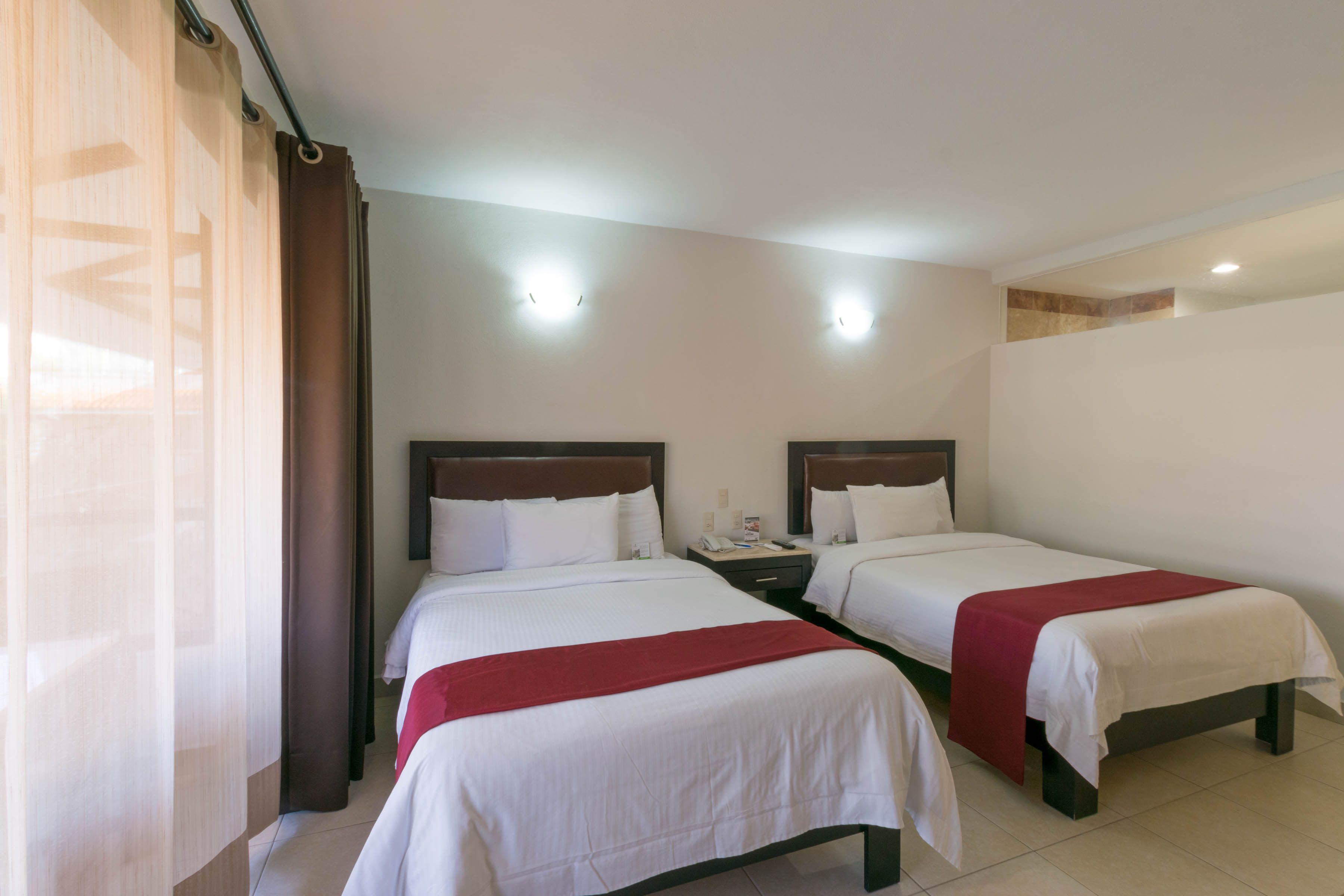 A hotel room with two beds, a nightstand, and a window with curtains.