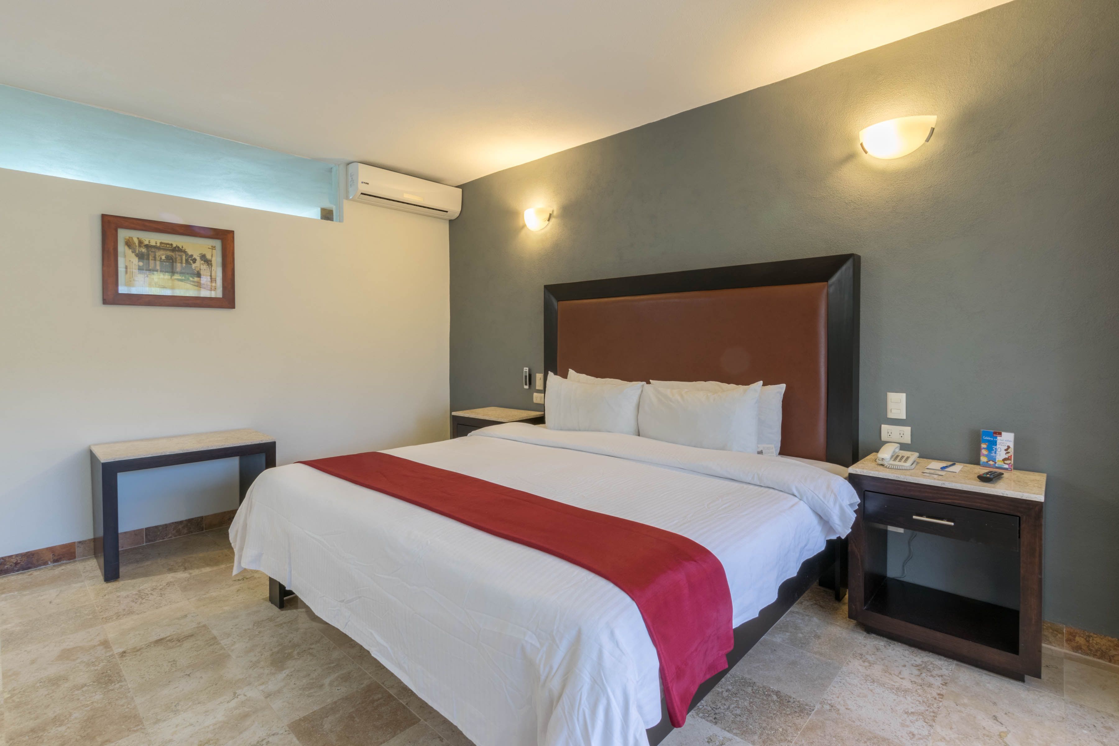 A hotel room with a large bed, a bedside table, a nightstand, and a wall-mounted light.