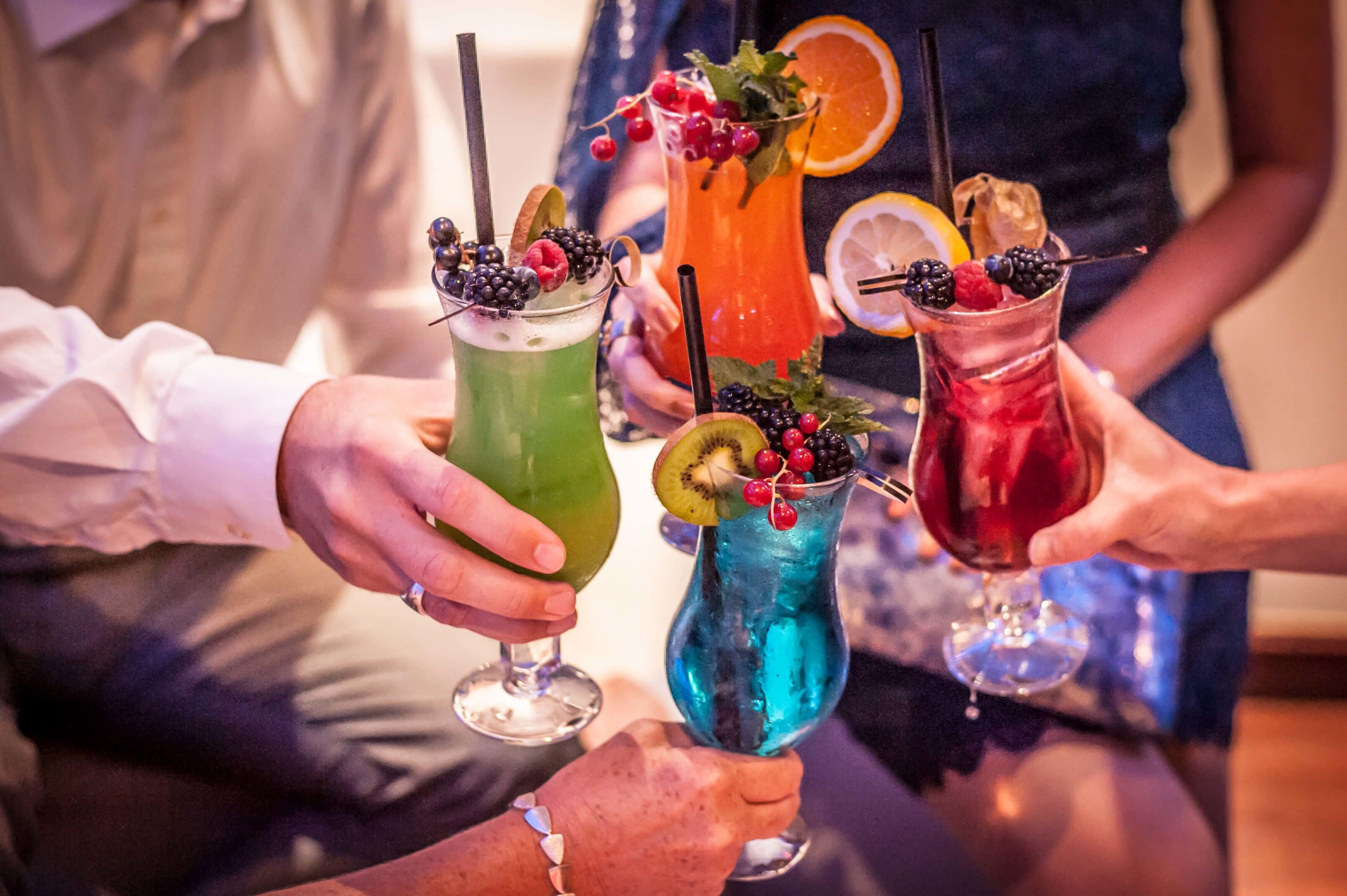 Un grupo de personas sosteniendo bebidas coloridas con frutas y adornos.