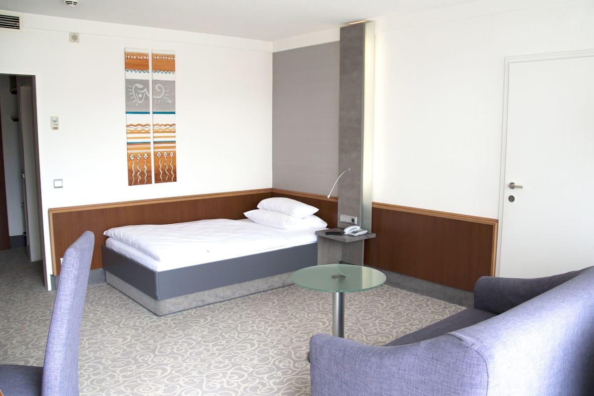 Una habitación de hotel con una cama, una mesita de vidrio, una silla y una pared con paneles decorativos.