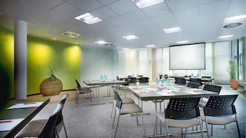 Un salón de conferencias con varias mesas, sillas y una pantalla para proyector.