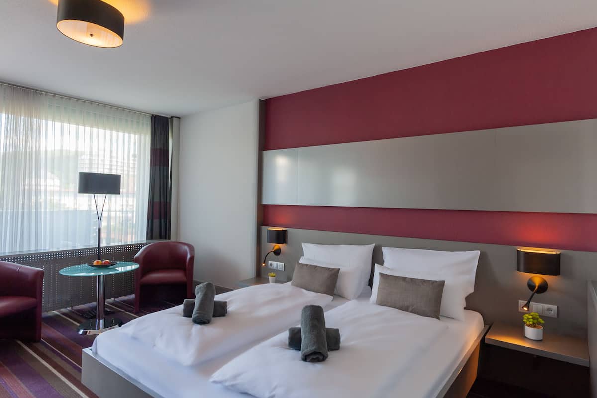 Habitación de hotel con una cama grande, dos mesitas de noche, un escritorio con silla, televisor y ventana con cortinas.