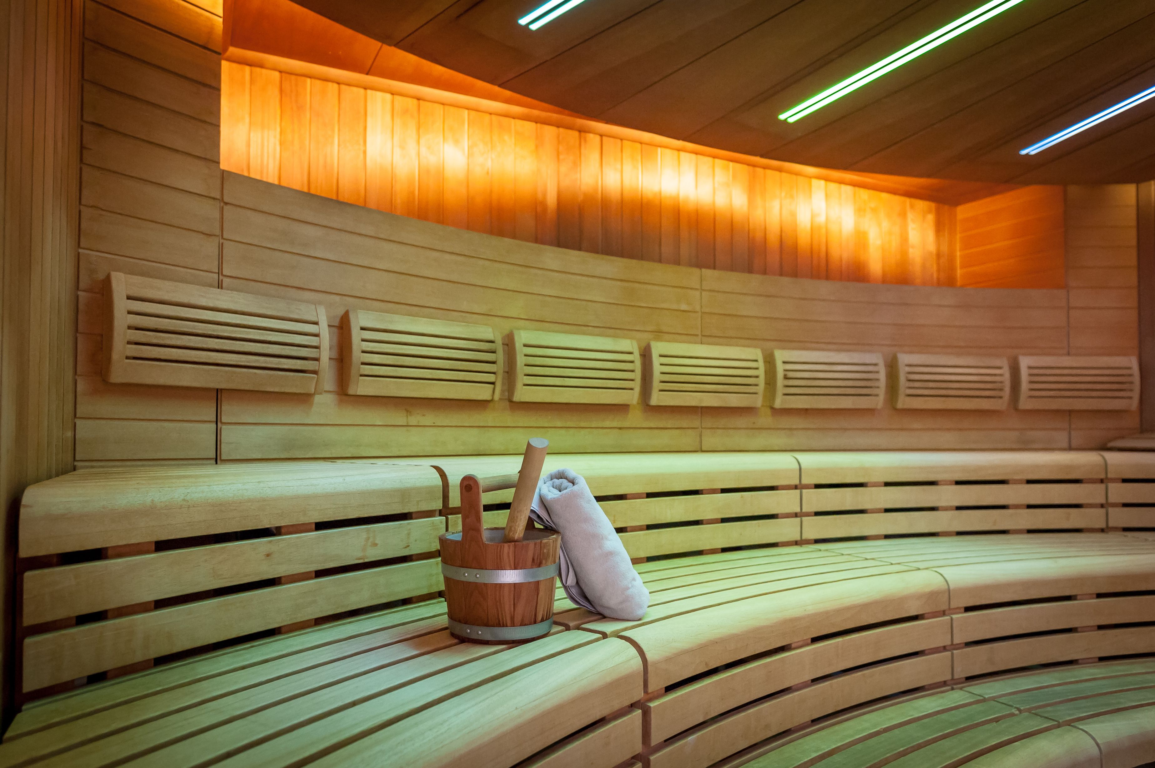 A sauna with wooden benches and a wooden bucket with a towel and a wooden mallet.