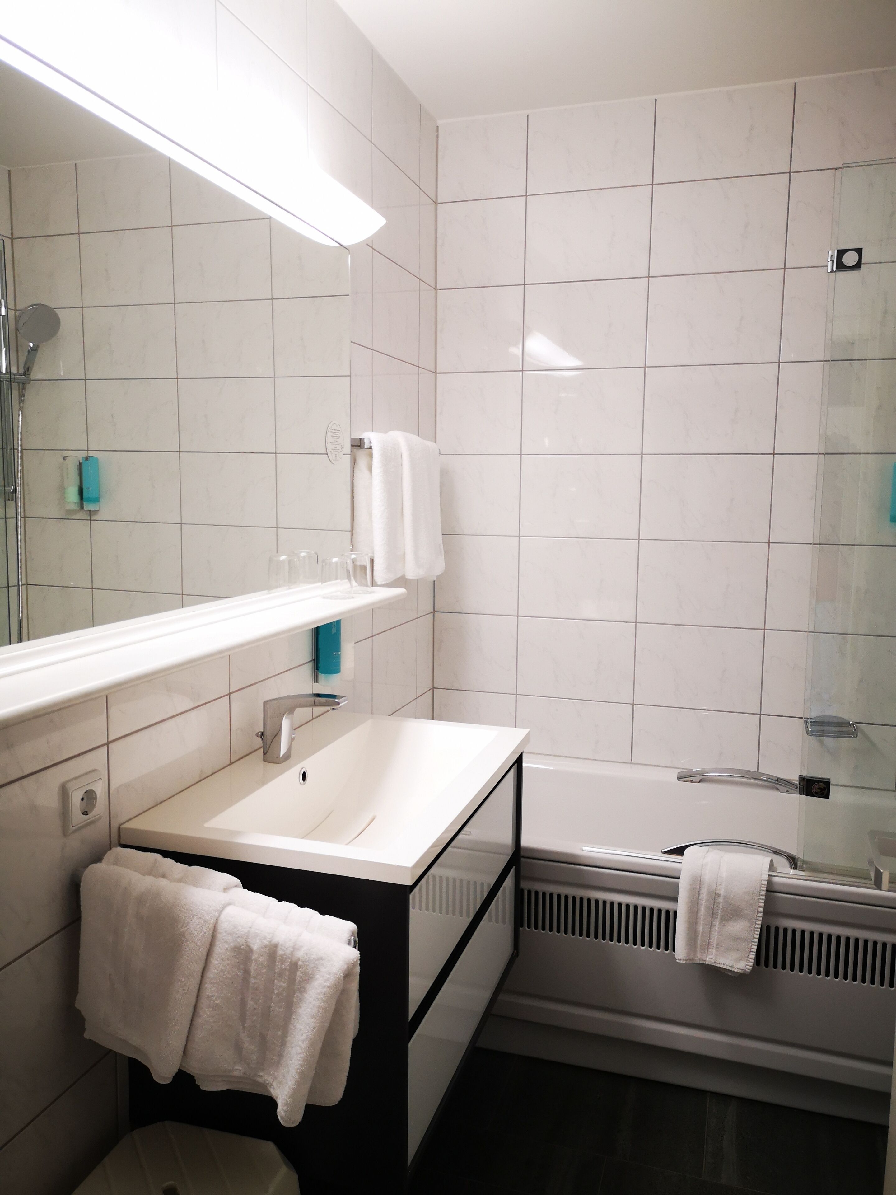 Une salle de bain moderne avec un lavabo blanc, un miroir et un espace douche.