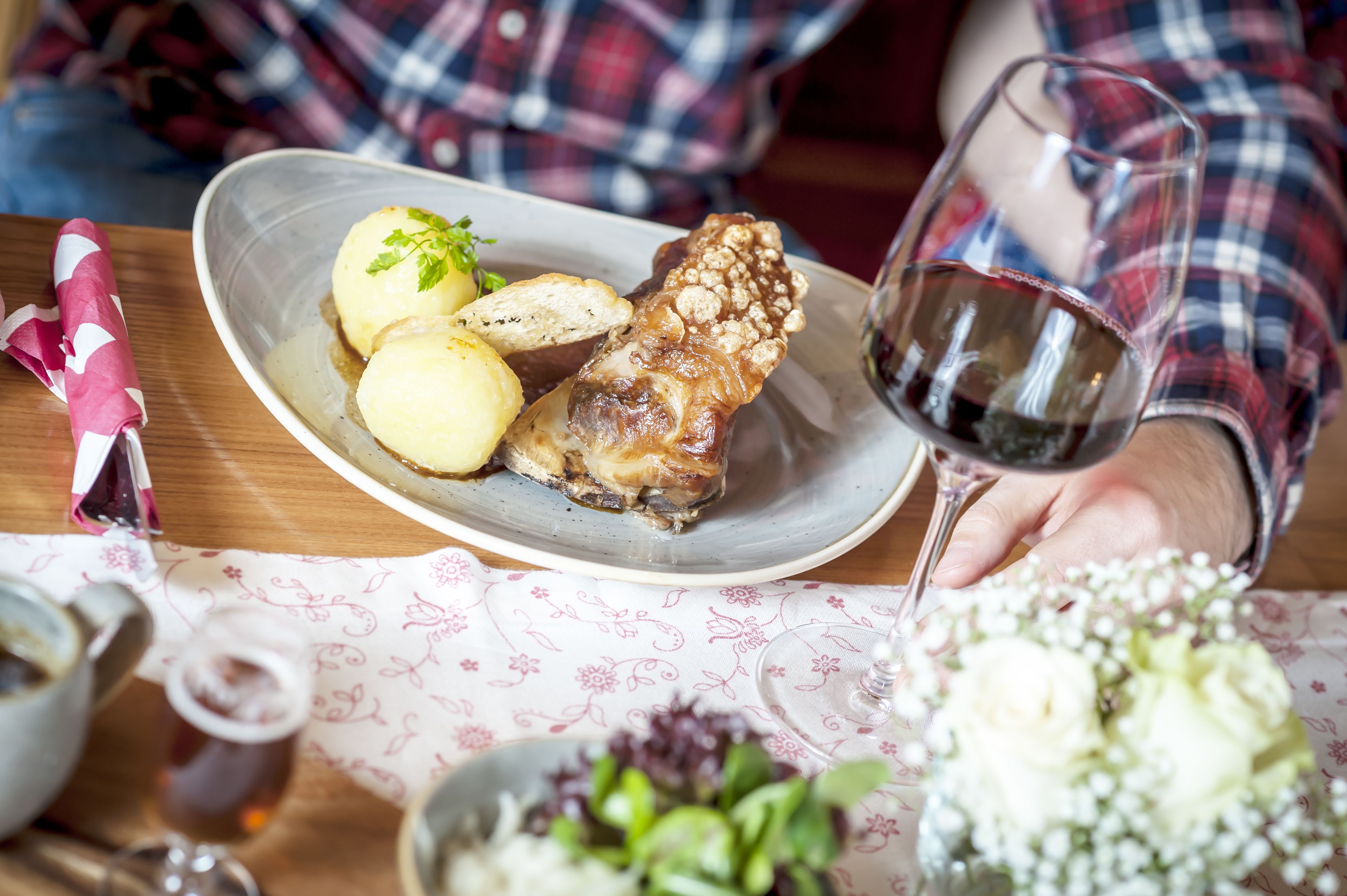 A dining table with a plate of food, a glass of red wine, and a floral tablecloth.