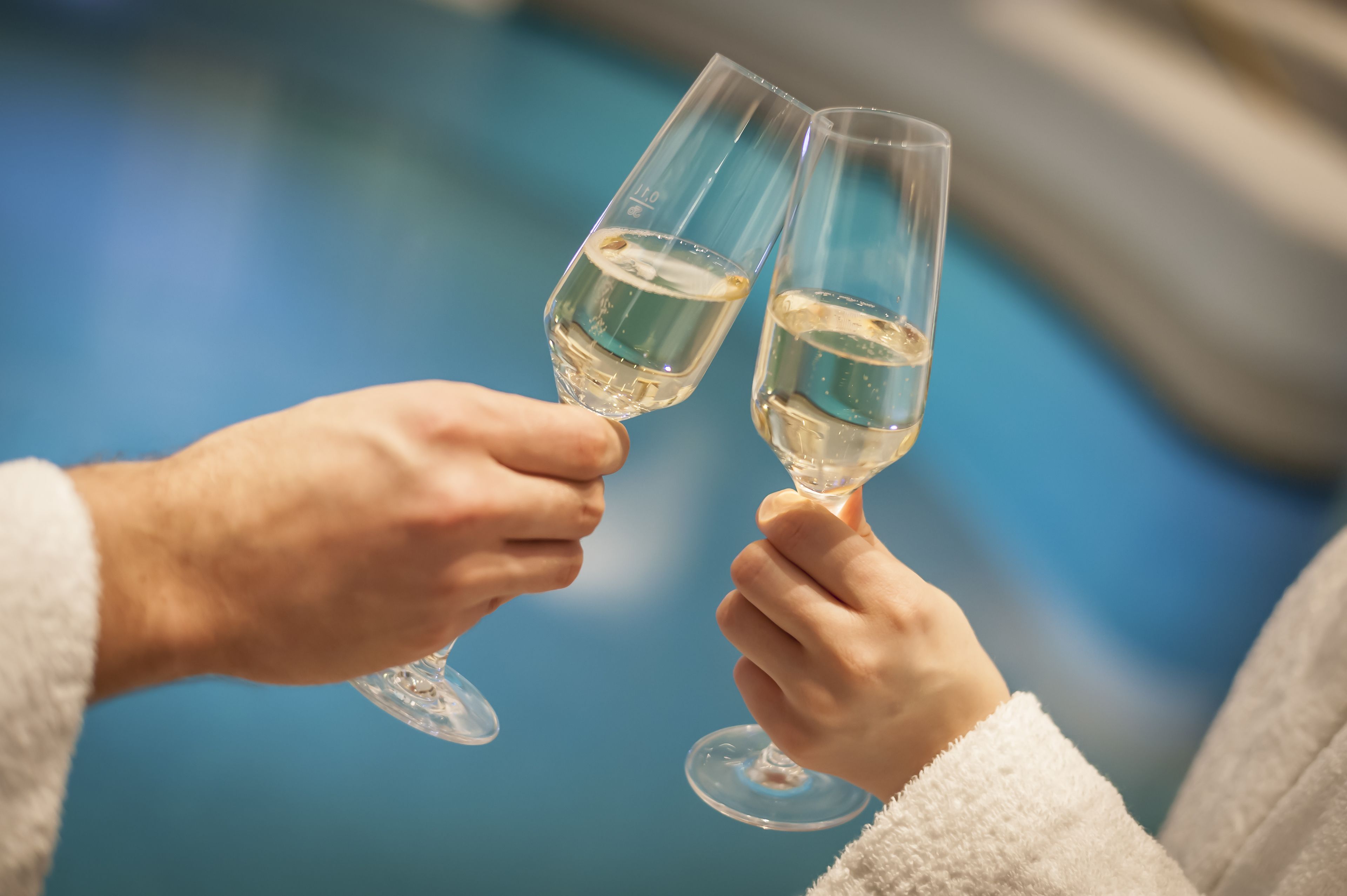 Dos manos sosteniendo copas de vino sobre un fondo azul.