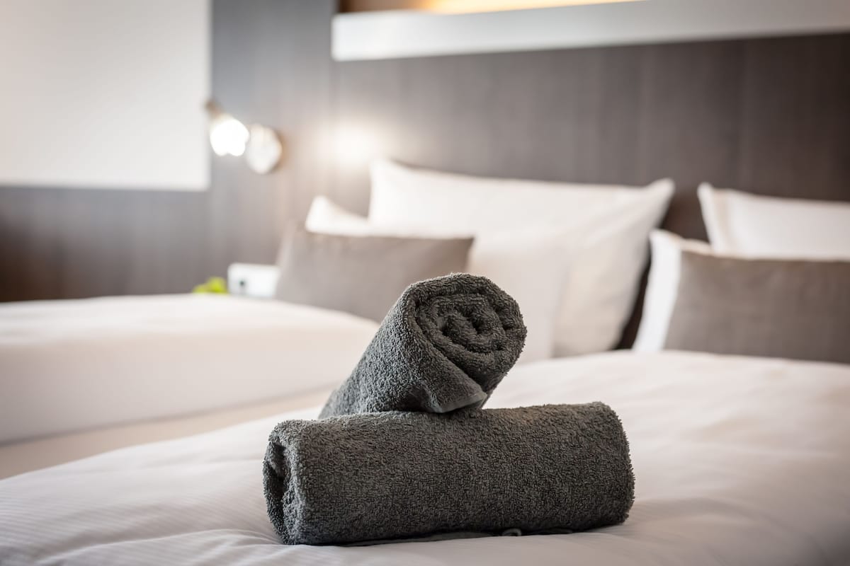 Una cama bien hecha con toallas enrolladas y almohadas en una habitación de hotel.