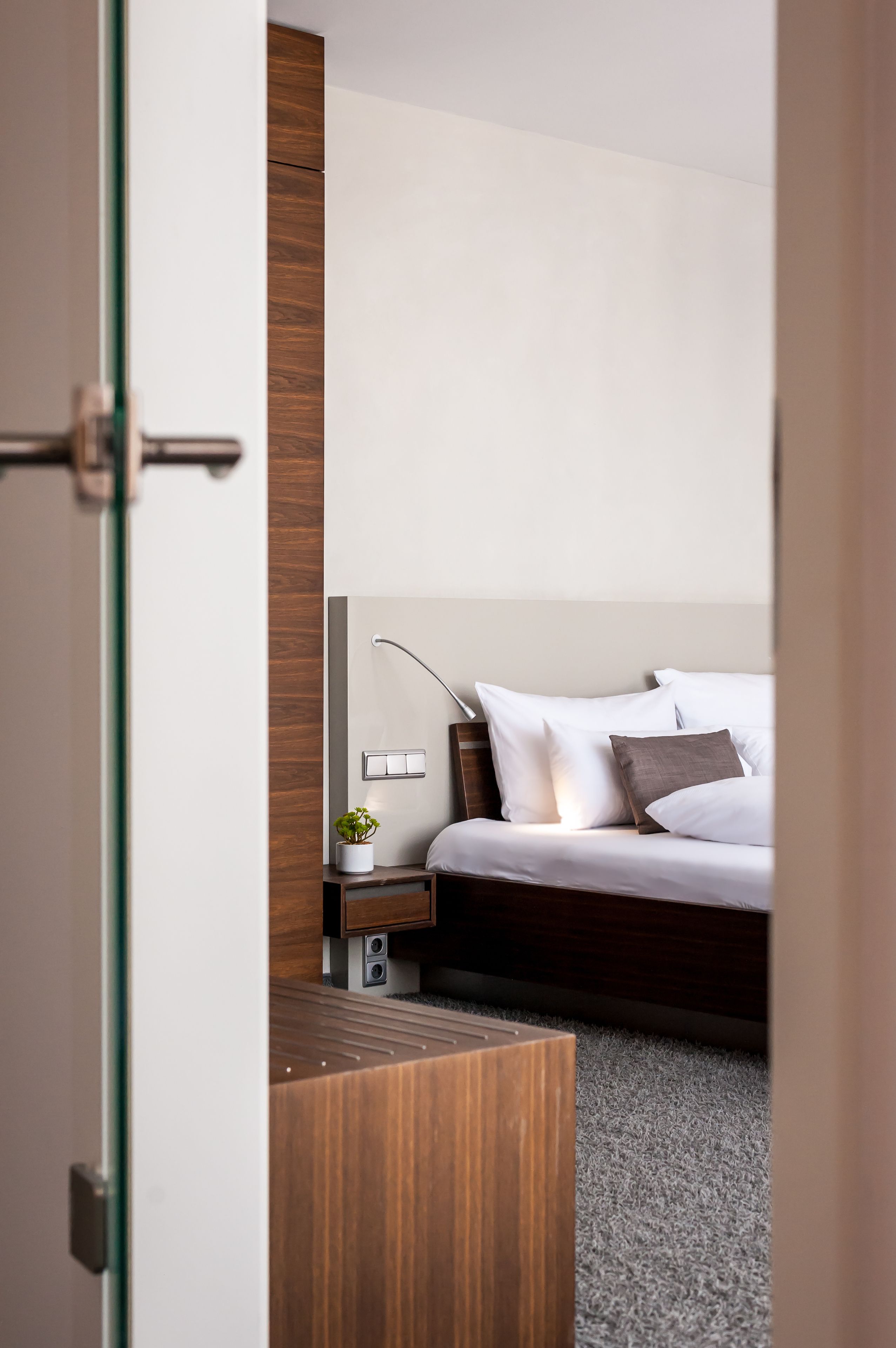 Ein modernes Hotelzimmer mit einer Wand aus Holzpaneelen, einem Bett mit weißer und brauner Bettwäsche, einem Nachttisch mit einer Lampe und einem kleinen Topfpflanzen.