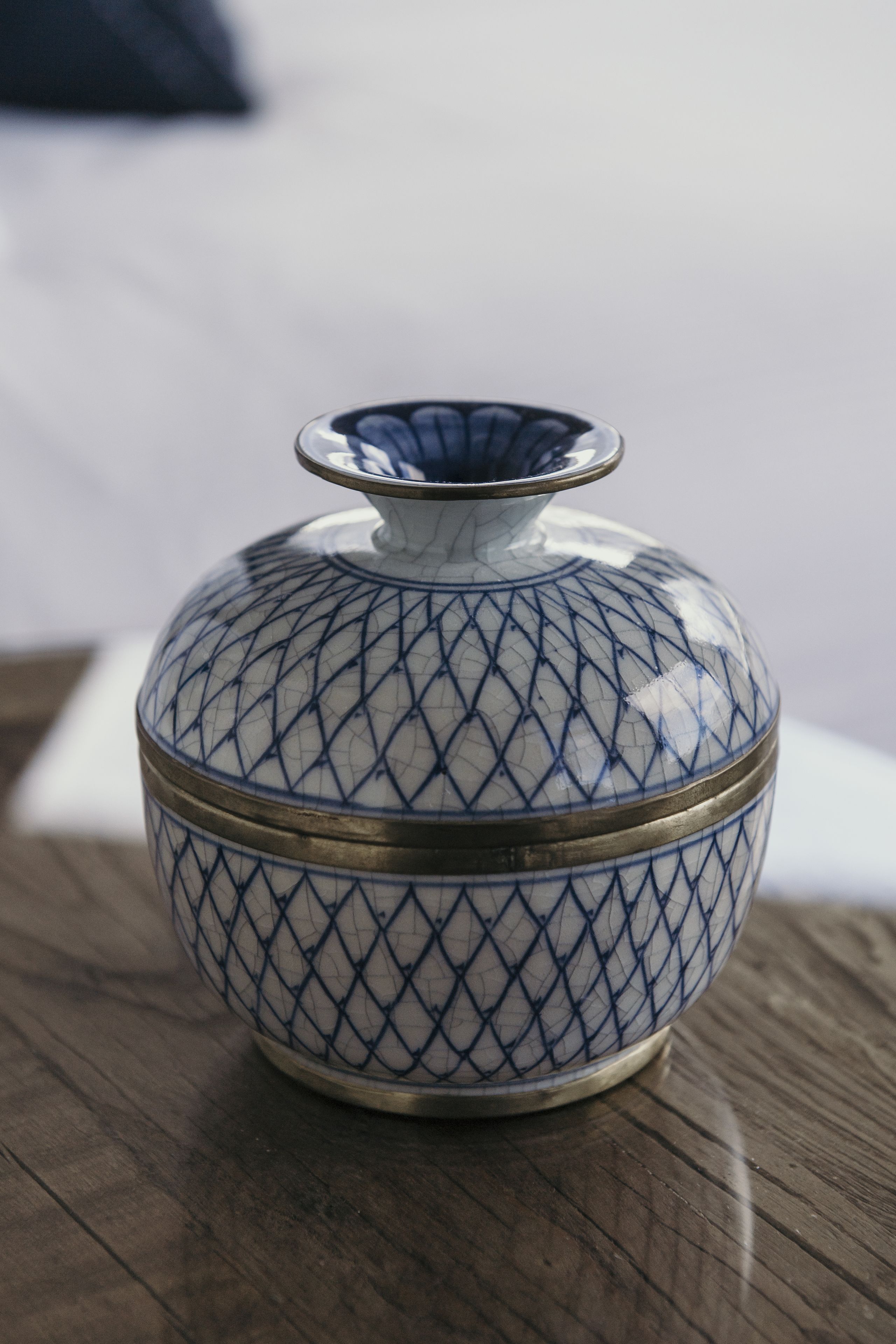Um vaso de cerâmica com padrão geométrico e faixa metálica, sobre uma superfície de madeira.