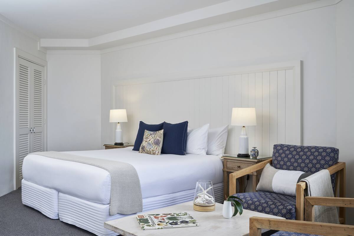 A neatly arranged hotel room with a large bed, two bedside tables with lamps, a chair, and a small table with a book and decorative items.