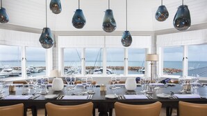 A dining area with a view of the marina, large windows, and hanging pendant lights. - Anchorage Port Stephens (Corlette)