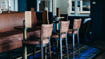 A modern lounge area with a leather sofa, bar stools, and a plaid carpet.