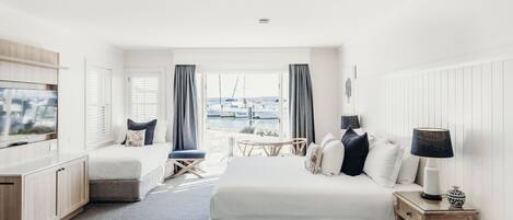A hotel room with a bed, a desk, a TV, a window with a view of boats, and a lamp.