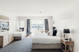 Habitación de hotel con cama, escritorio, televisión, ventana y vistas a barcos, además de una lámpara.